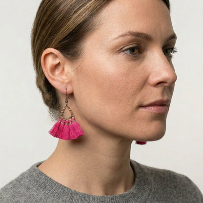 Aramat Jewels boho oorhangers met fel roze kwastjes en bronskleurige metalen details gedragen door een model.