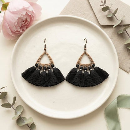 Aramat Jewels boho oorhangers met zwarte kwastjes en bronskleurige metalen details op een keramisch bord.
