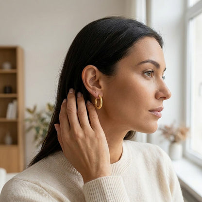 Aramat Jewels gold-tone twisted, diamond-cut stainless steel hoop earrings, 20mm diameter, worn by a woman.