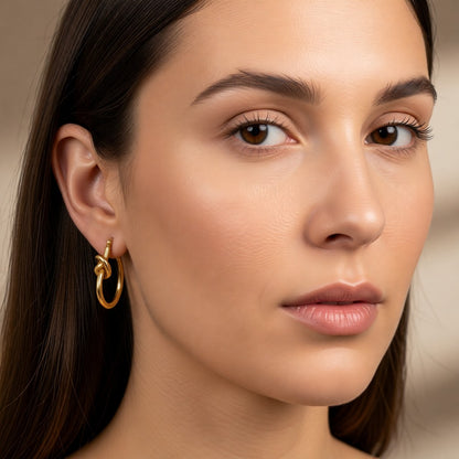 Aramat Jewels gold-tone stainless steel hoop earrings with a knot detail, 25mm diameter.
