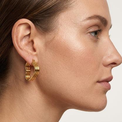 Aramat Jewels gold-tone triple heart hoop earrings with a hinged closure, worn by a model.
