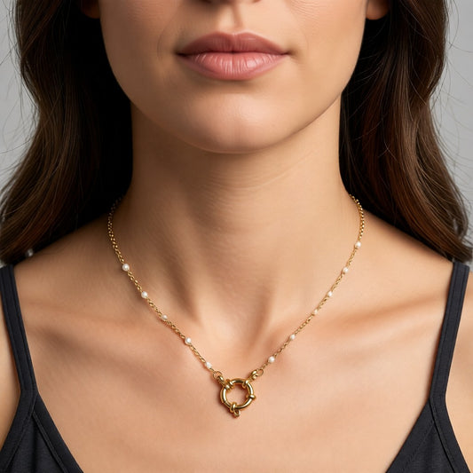 Aramat Jewels gold-tone stainless steel necklace with white enamel beads and a circular clasp, worn by a woman.