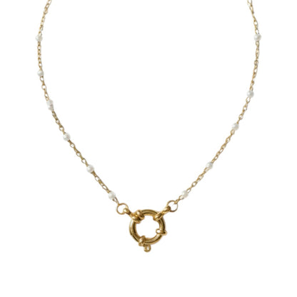 Aramat Jewels gold-tone stainless steel necklace with white enamel beads and a circular clasp, displayed on a branch.