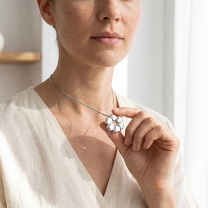 Aramat Jewels circular cremation pendant with heart details, made of stainless steel, worn by a woman.
