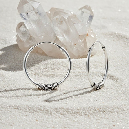 Aramat Jewels 18mm oxidized silver Bali hoop earrings with intricate detailing, styled on a sandy surface with crystals.
