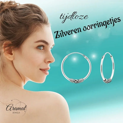 Aramat Jewels 20mm oxidized silver Bali hoop earrings with intricate detailing, worn by a woman.