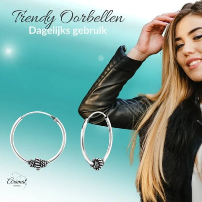 Aramat Jewels 18mm ethnic silver Bali hoop earrings with a textured knot detail. These oxidized silver earrings are shown on a model wearing a black leather jacket.