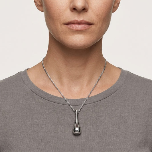 Aramat Jewels silver-colored 316L steel cone urn pendant on a rope chain necklace worn by a woman.
