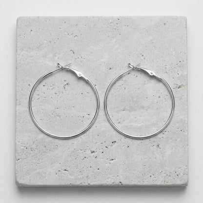 Aramat Jewels silver-coloured metal hoop earrings, 40mm diameter, with a hinge clasp. Lightweight and timeless.