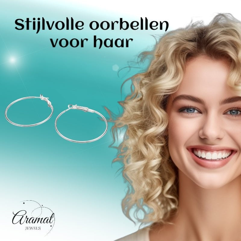 Aramat Jewels silver-coloured metal hoop earrings, 40mm diameter, with a click-top clasp. Model has blonde curly hair and blue eyes.