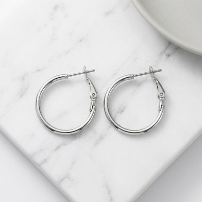 Aramat Jewels silver stainless steel hoop earrings with a high-gloss finish and hinge closure, available in multiple sizes.
