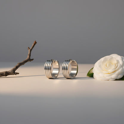 Aramat Jewels silver-tone stainless steel hoop earrings with three subtle vertical stripes, available in 13mm and 20mm diameters.