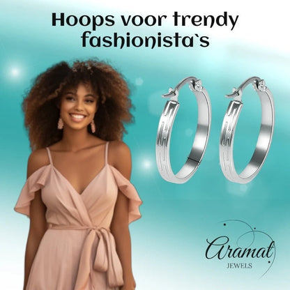 Aramat Jewels silver stainless steel hoop earrings with a striped pattern, 20mm diameter, worn by a smiling woman in a light pink dress.