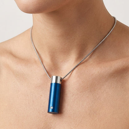 Aramat Jewels stalen blauwe cilinder ashanger met een klein diamantje, gedragen aan een zilverkleurige slangenhalsketting.