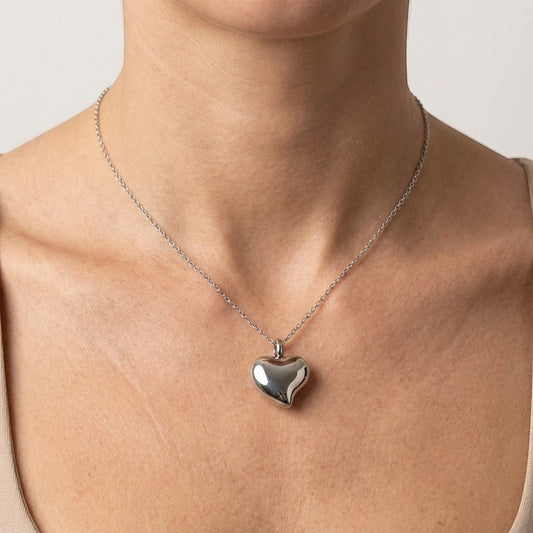 Aramat Jewels zilverkleurige hartvormige crematiehanger van roestvrij staal, gedragen aan een fijne ketting.